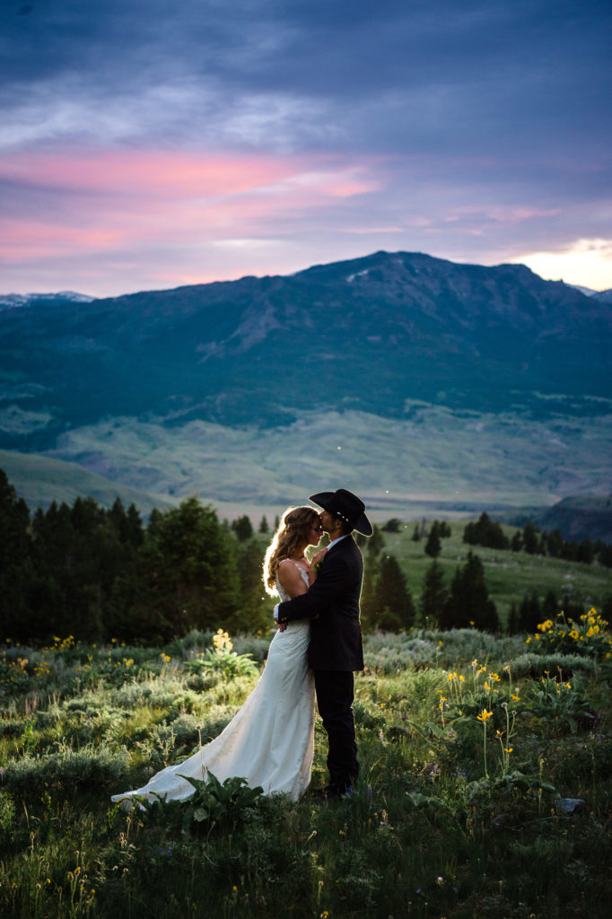 Montana elopement guide with husband kissing brides forehead in Yellowstone National park with pink and purple sky. 