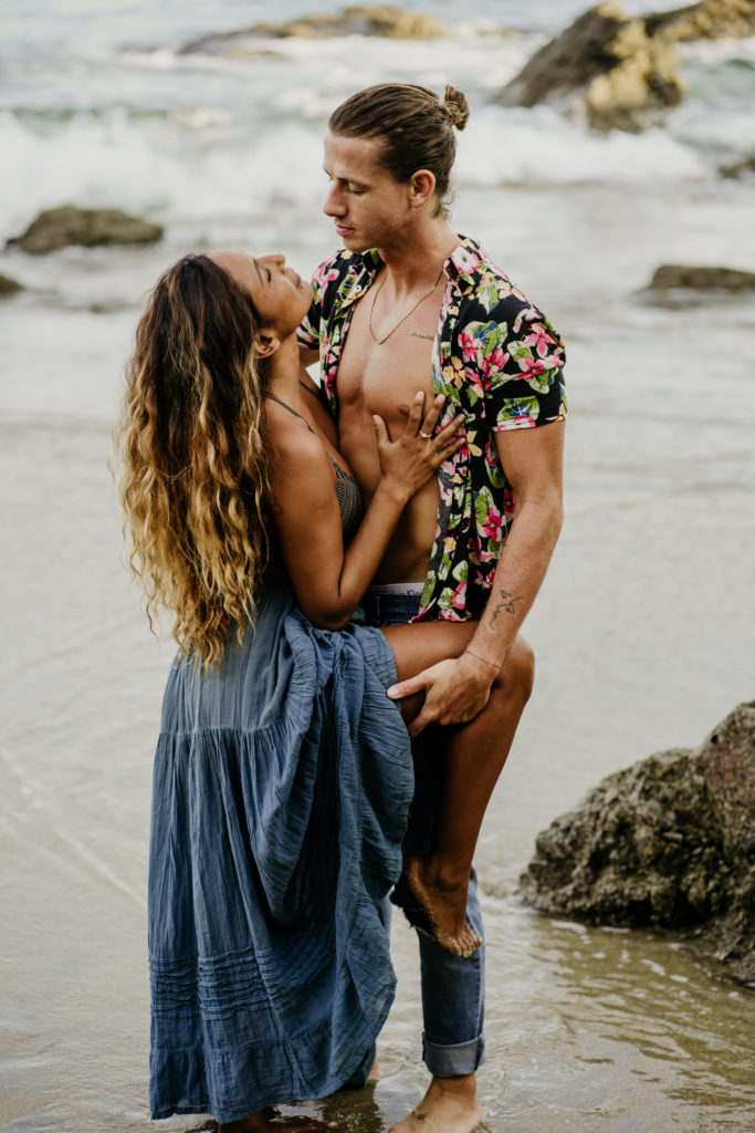 Top Elopement Destinations: Talum. Man holding woman's leg up as she presses a hand against his chest. The ocean water covering their feet. 