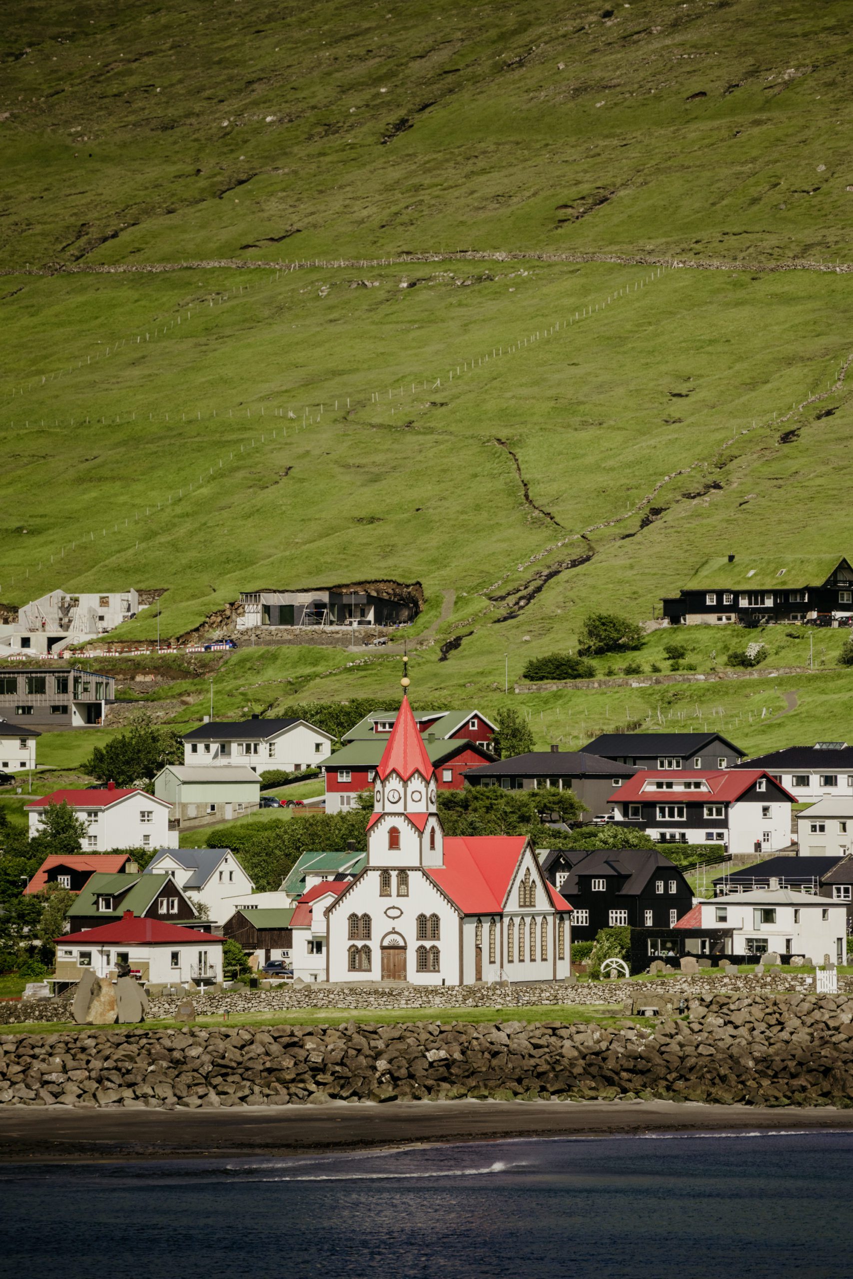How to elope in Faroe Islands. The village Sandavágur is situated on Vágar island. red roof church in Sandavagur. 