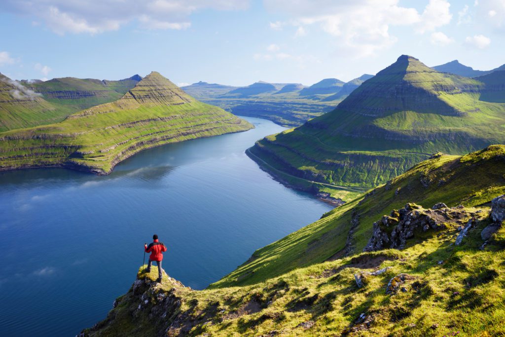 how to elope in Faroe Islands. View on Funningur fjord from the Funningur top. Eysturoy Island, Faroe islands. Tourist in a red jacket explores natural attractions. Summer mountain landscape