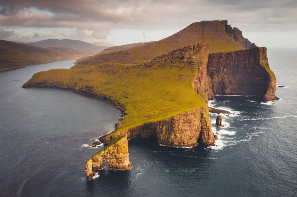 how to elope in Faroe Islands. Famous Drangarnir Rock Formation in the North Atlantic Ocean in warm golden sunset light. Aerial Drone Point of view of the iconic Drangarnir Rock Formation between the Islet Tindholmur and Vágar Island, Faroe Islands, Denmark, Nordic Countries, Europe