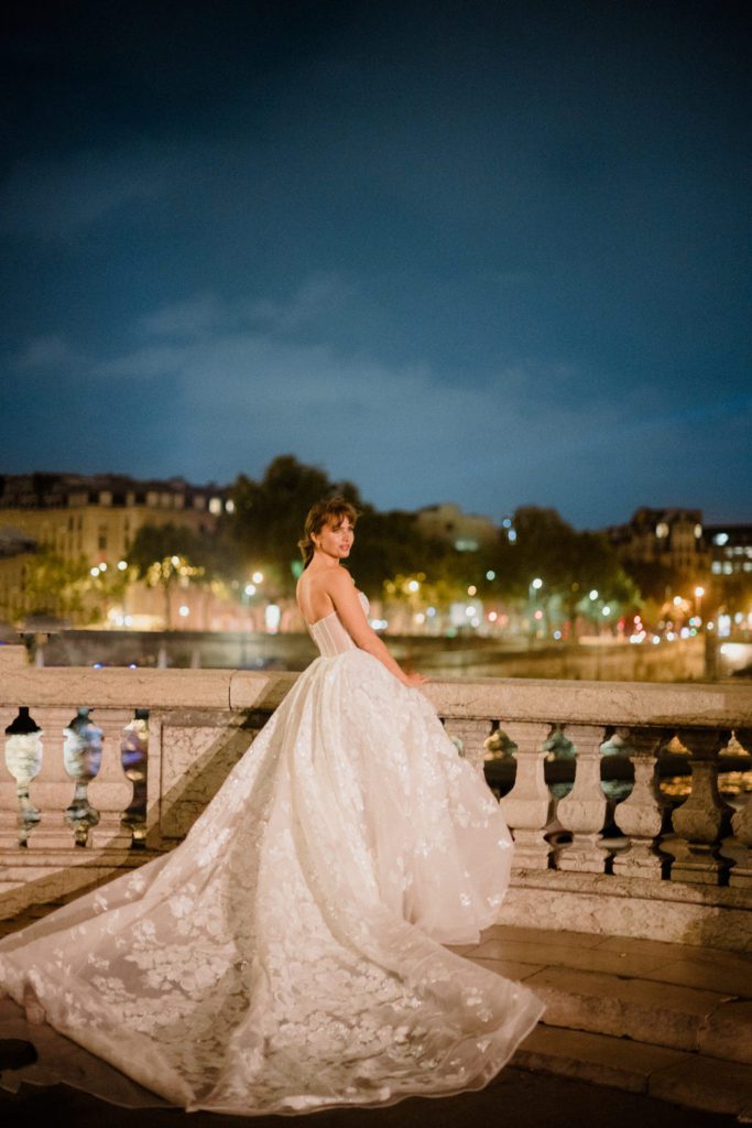 Top Elopement Destinations, France. Bride in a wedding gown on a bride with Paris lights in the background. 