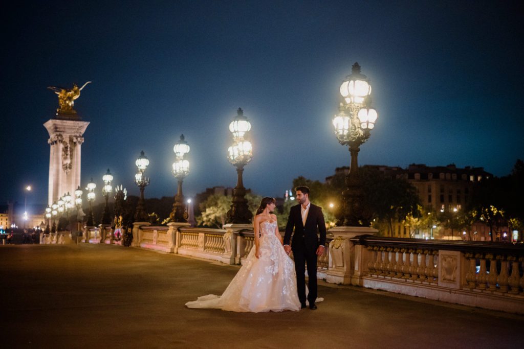 Everything you need to know about vow renewals. Couple in Paris dressed for a wedding, walking along the bridge. 