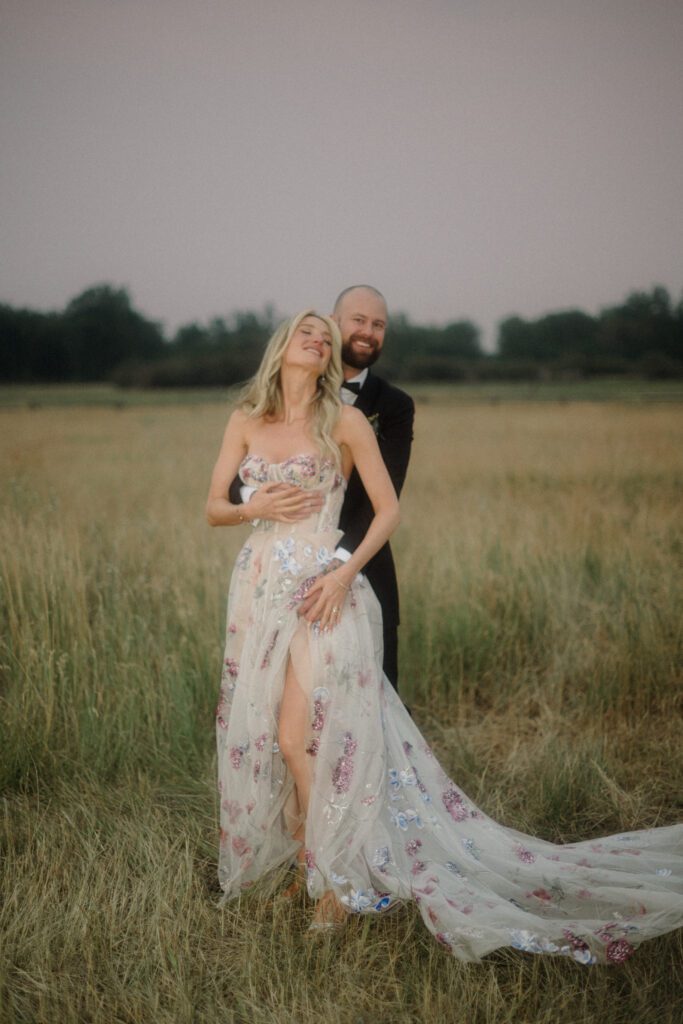 Montana elopement guide with husband holding bride in gorgeous white floral dress. In the middle of a field. 