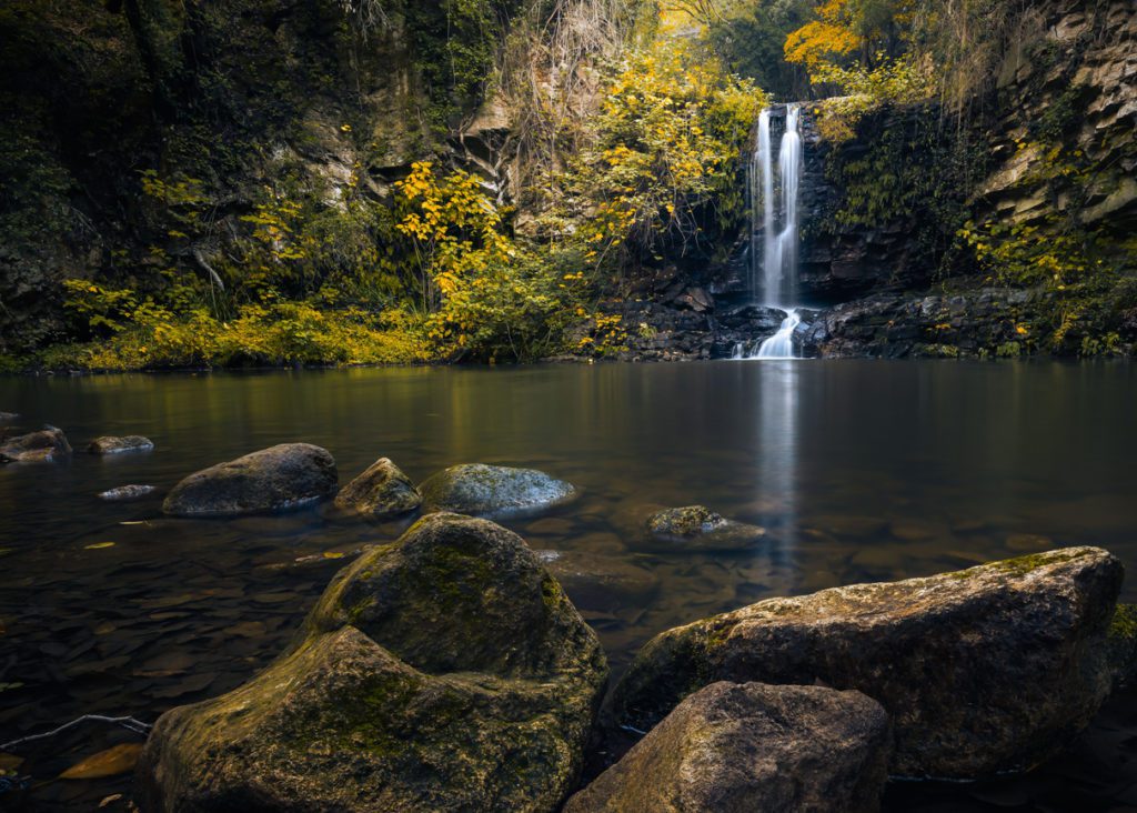 A waterfall in Cerveteri, Italy falling from a cliff into a lagoon with trees and rocks around