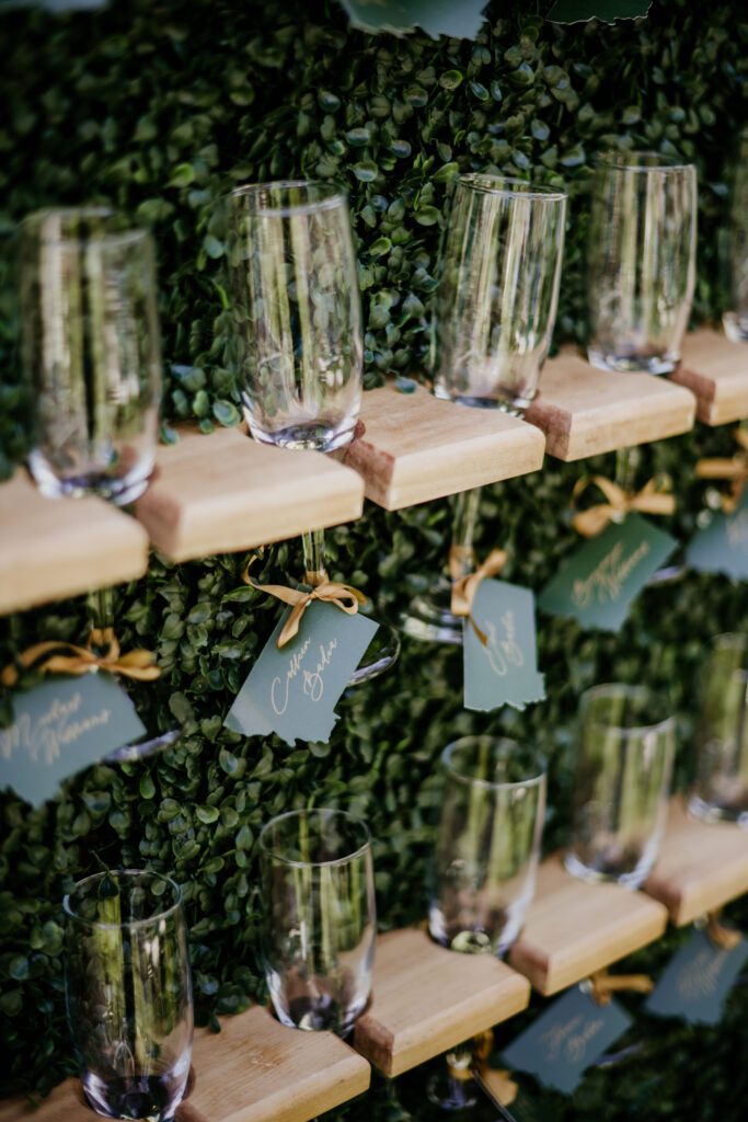 Champagne wall seating chart with escort cards on champagne glasses. Luxury Montana wedding. Emerald greens + burgundy details dress up the Montana mountains. Alpine Falls Ranch wedding checks all the boxes for a destination wedding.