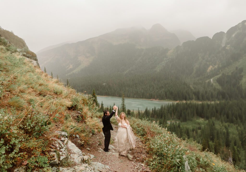 Many Glacier Hotel Micro Wedding couple hikes to Grinnel Glacier on the east side of the park. The rain is coming down and Grinnel Lake is in the background.