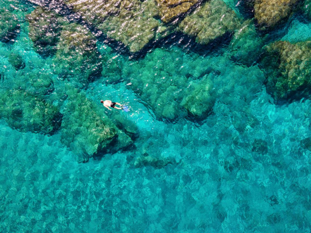 A man snorkeling ( a great Greece elopement activity!) in the emerald waters of the Aegean Sea in Andros island, Cyclades, Greece, during summer time