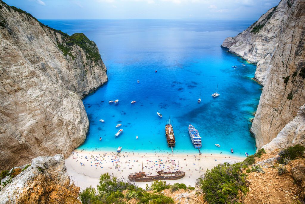 
Tourists and tourist boats  in the famous Navagio Bay, Zakynthos island, Greece. The beach of Navagio with the old shipwreck is one of the main tourism spots of Zakynthos island in Greece - beside of the wreck its the turquoise sea what makes this place so famous.