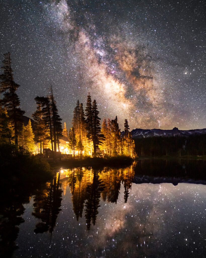 The Milkyway Galaxy casts its reflection in Twin Lakes (at Mammoth Lakes). Calm yet fiery lights on the forest. Shot on Sony A7C 12:30am