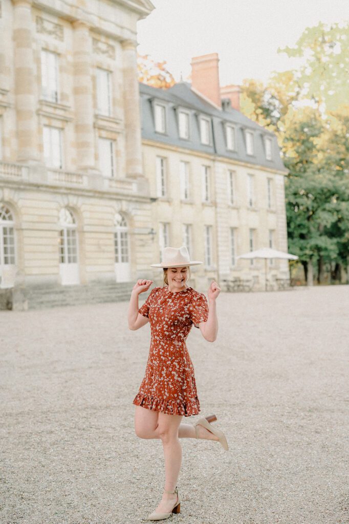 How to keep your sanity as a business owner! Entrepeneur in France having fun with one leg kicked up in a red floral dress and white brimmed hat.