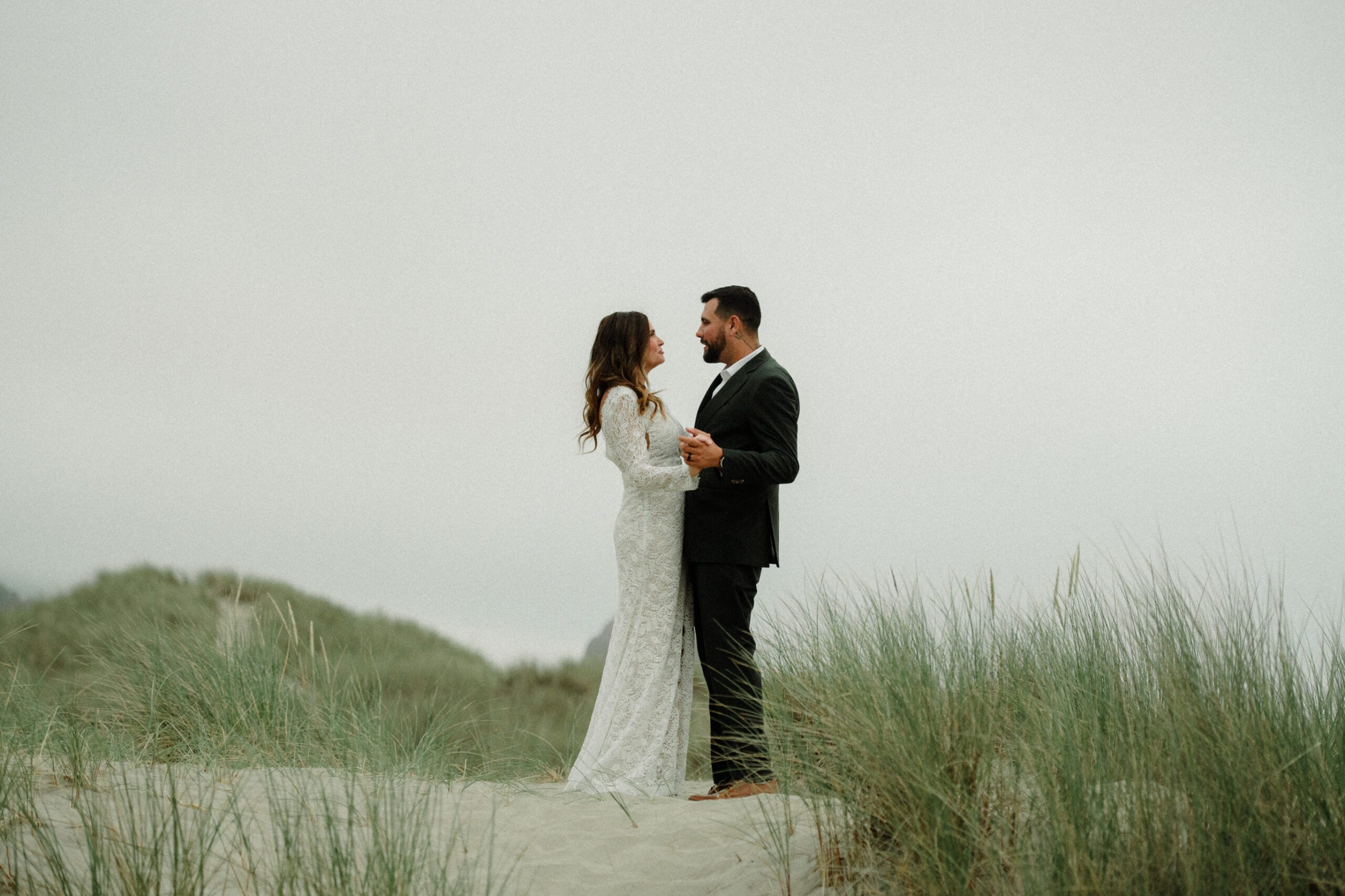 The total cost to elope in Cannon Beach includes location, officiant, bridal styling, a photographer, and where you want to stay! Photo holding hands and staring into each other's eyes on the Oregon Coast.
