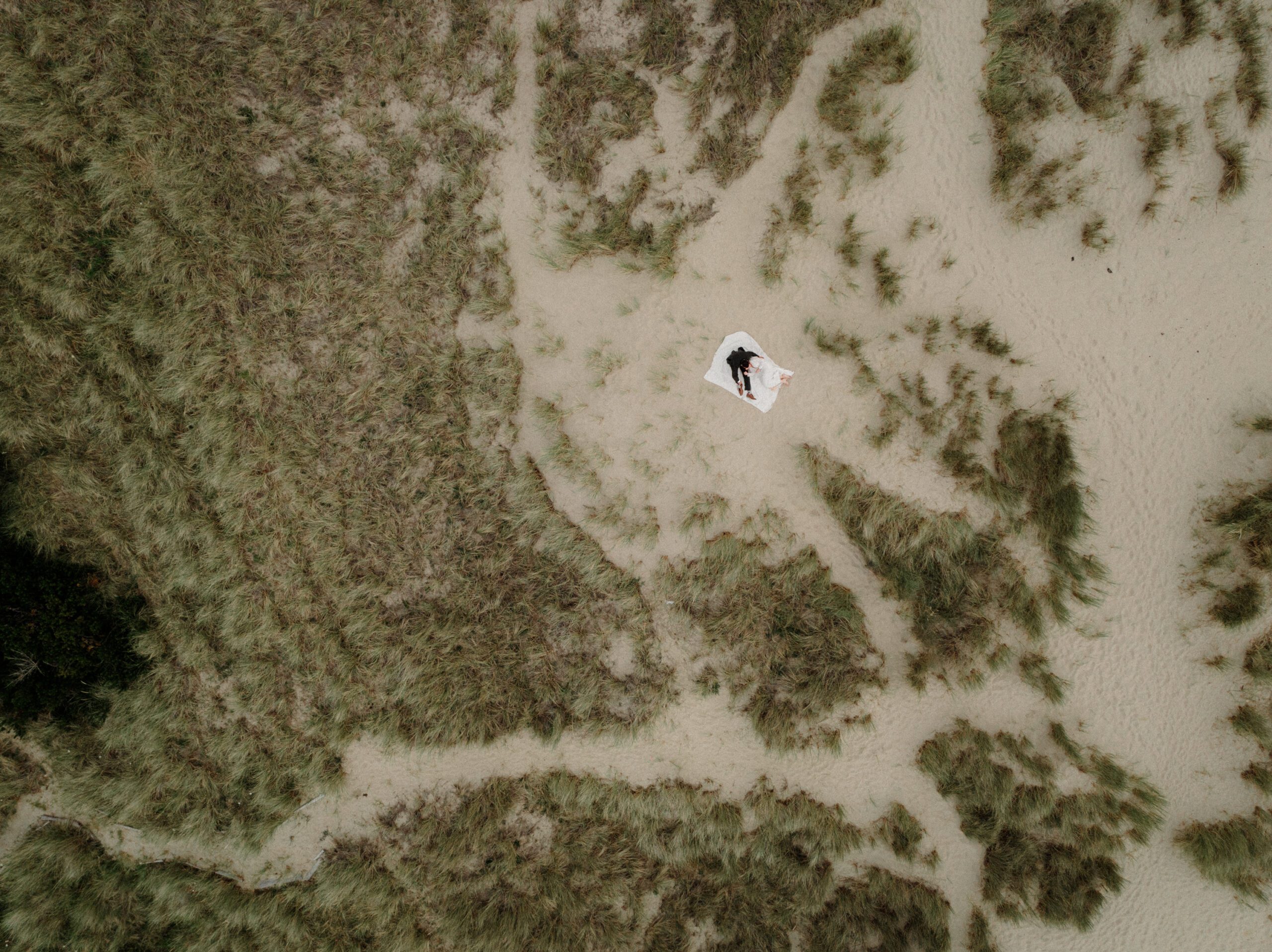 Drone footage of a couple lying on a white blanket on the Oregon shore at Cannon Beach in Oregon.
