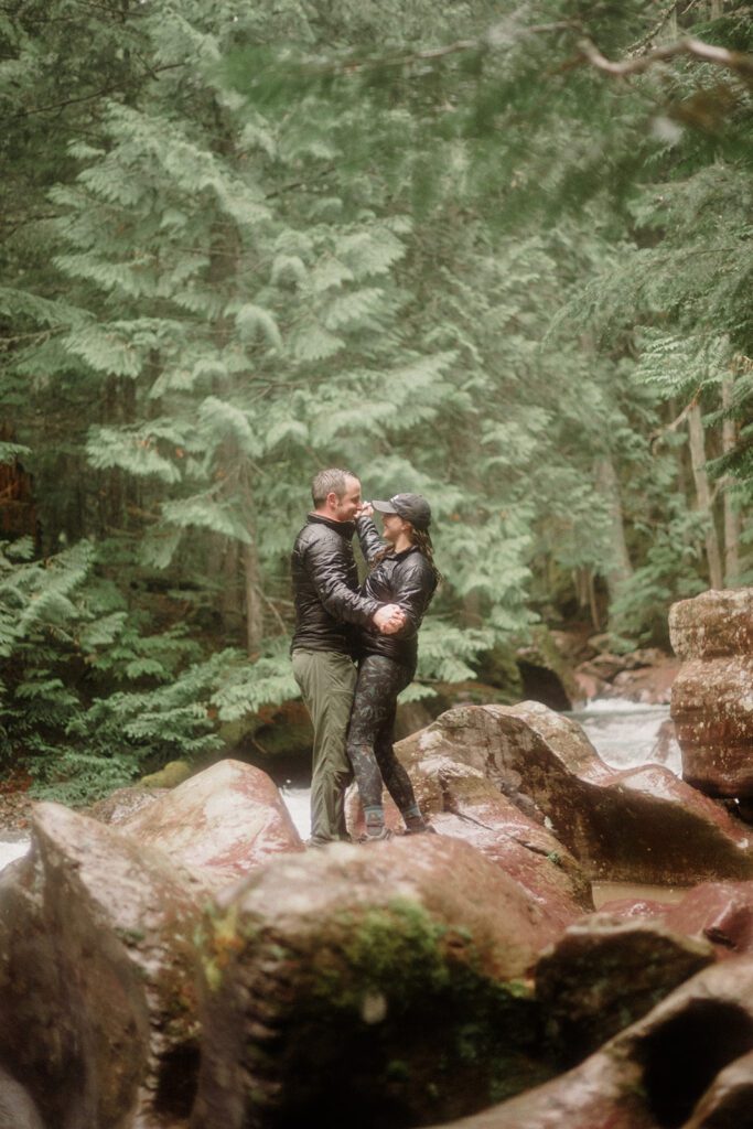 Couple on rocks with massive trees behind them holding each other.