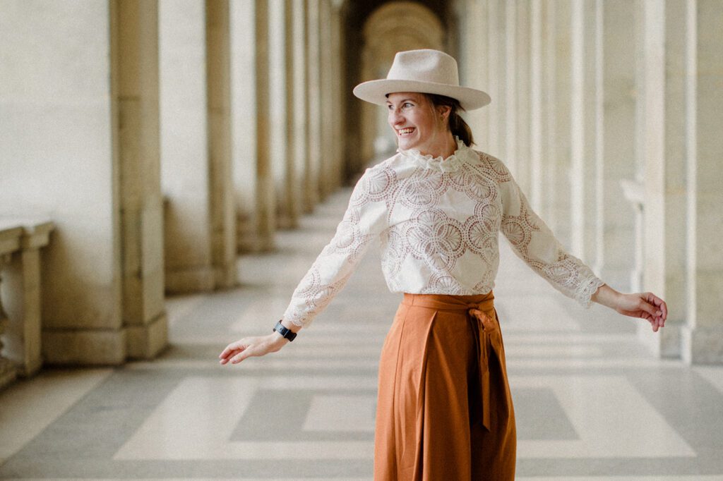 KPIs as a photographer, woman in white blouse, burnt orange pants, white brim hat, in Paris.