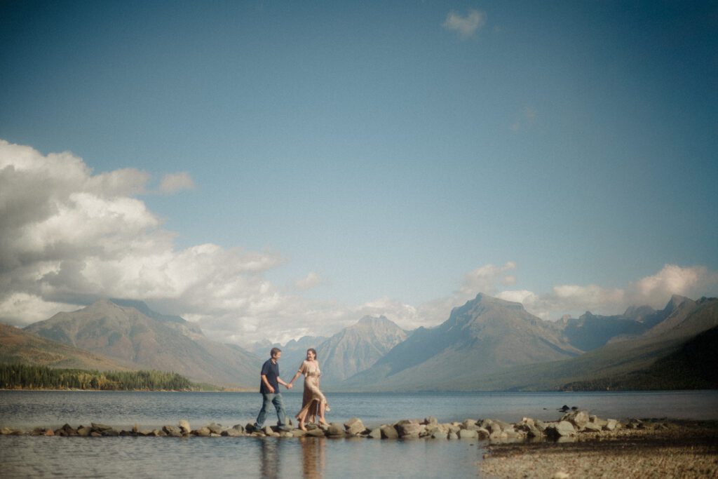 Couple walking across rocks holding hands at Lake McDonald Glacier National Park .