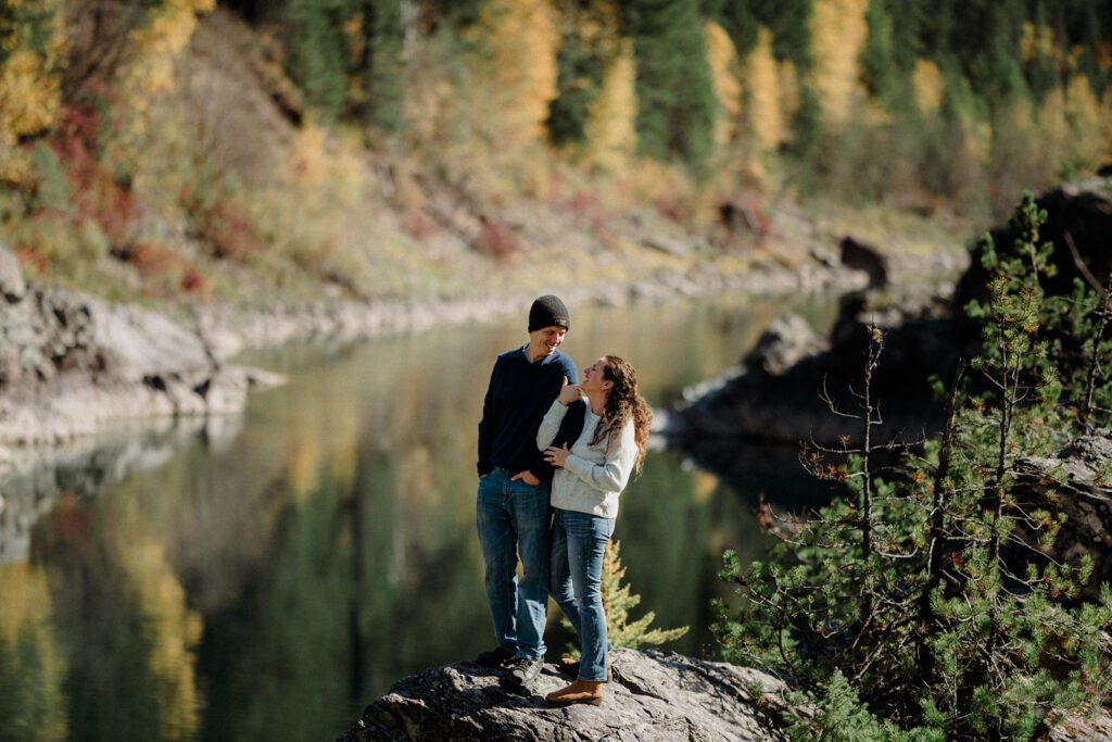 Man looking down at wife while the couple stand on a rock next to a river.