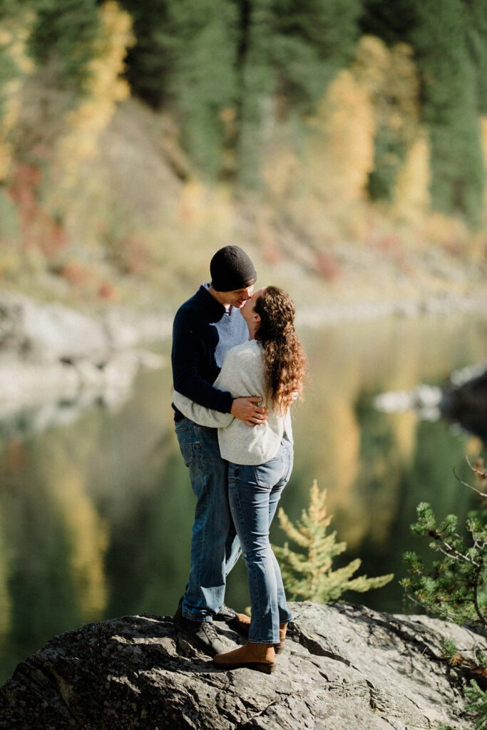 Couple nose to nose in autumn with color changing trees and river in background.