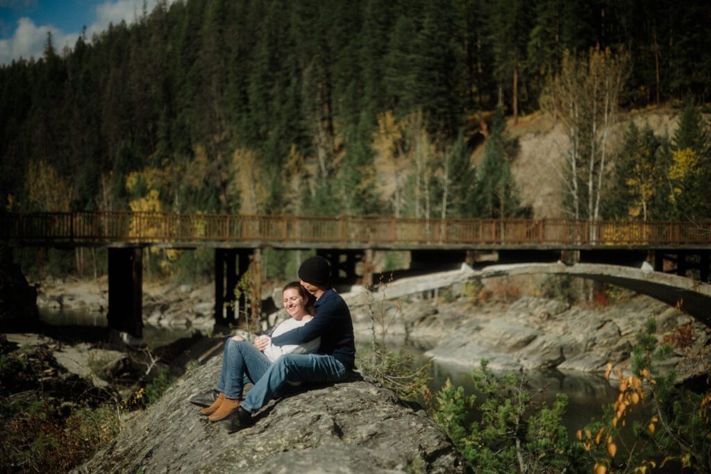 Man holding woman on a rock with bridge in the background.