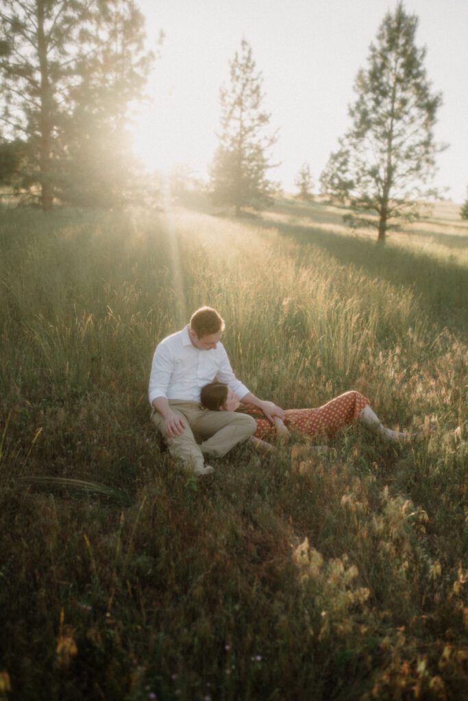 A couple laughs while looking at each other during engagement photos in Missoula. A river is behind them and trees are featured.