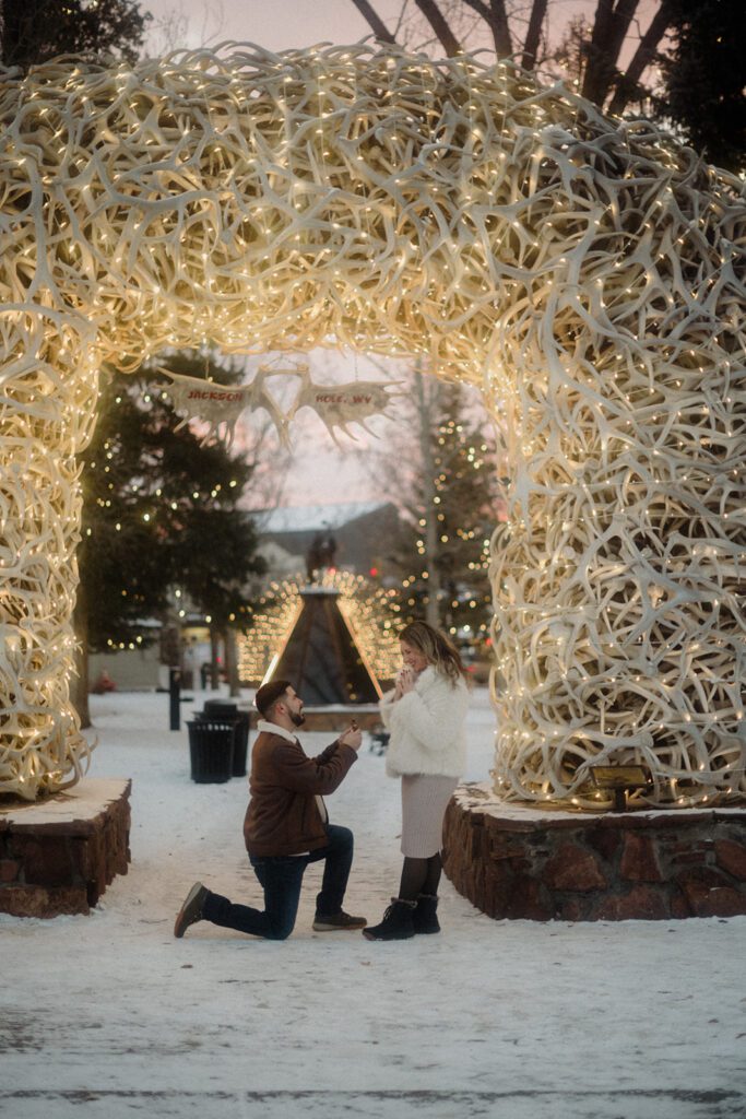 Surprise proposal in Jackson Hole, Wyoming in the snow. Man on his knee and woman looking delighted. 