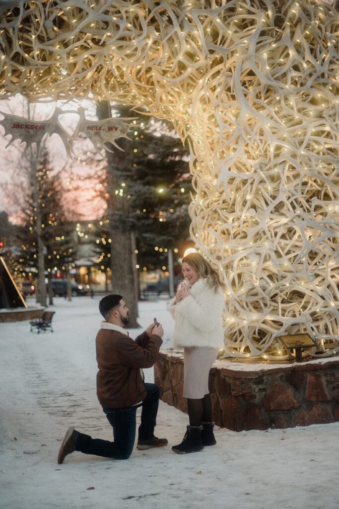 Surprise proposal in Jackson Hole, Wyoming in the snow. Man on his knee and woman looking delighted. 