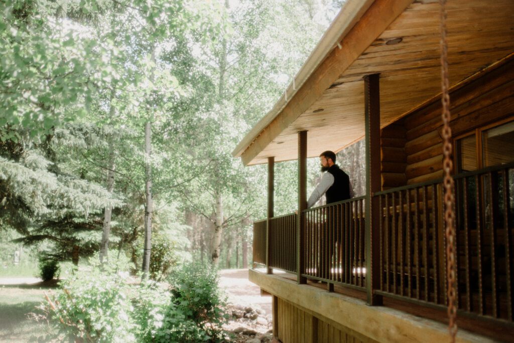 Groom looking out on second story balcony into trees before he marries the love of his life in Glacier National Park.