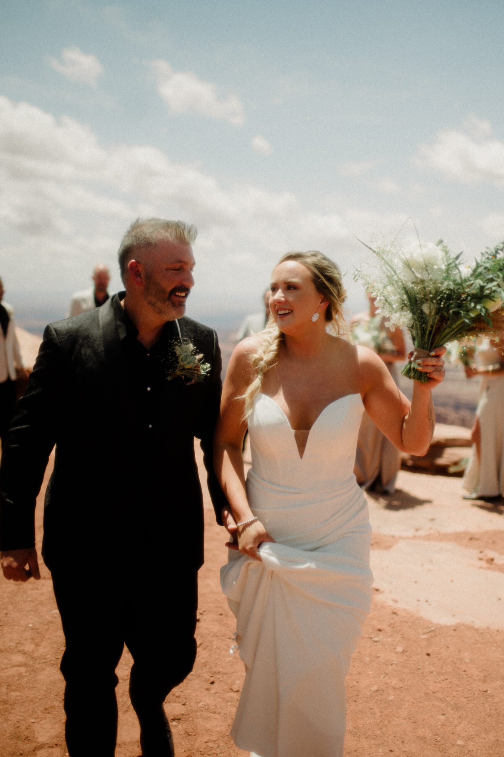 Moab, Utah adventure wedding with bride and groom walking down the aisle. Summer sun above and red rocks below. 