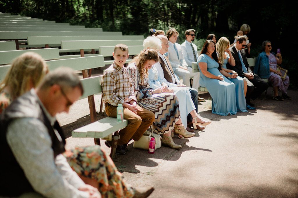 Apgar Ampitheater, Glacier National Park. How to have a micro wedding. Guests waiting on faded green bench seating for the ceremony