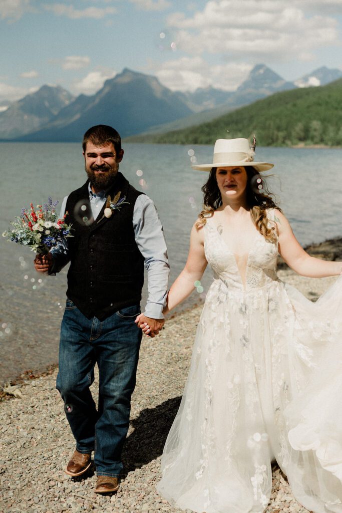 Bride and groom holding hands on the shores of Lake McDonald with water spots on the camera.