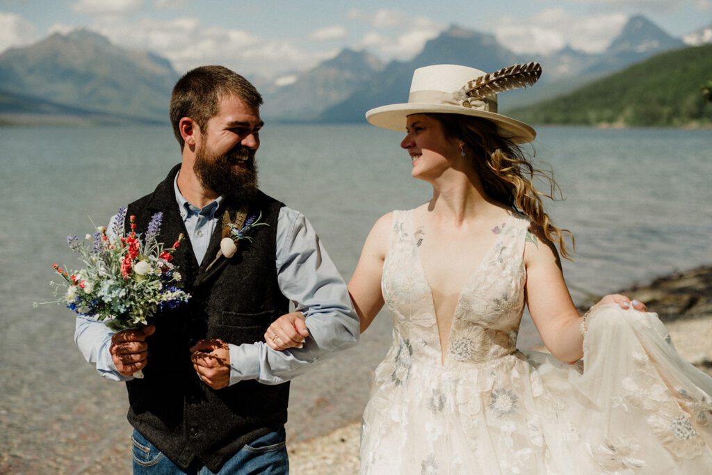 Bride and groom with arms interlocked on the shores of Lake McDonald.