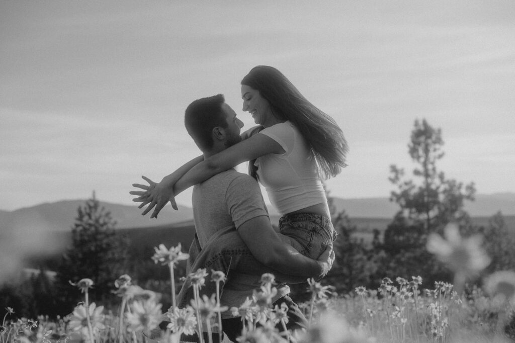 Proposal advice to get the YES! Blank and white photo of man picking up his new fiancé in a flower field.