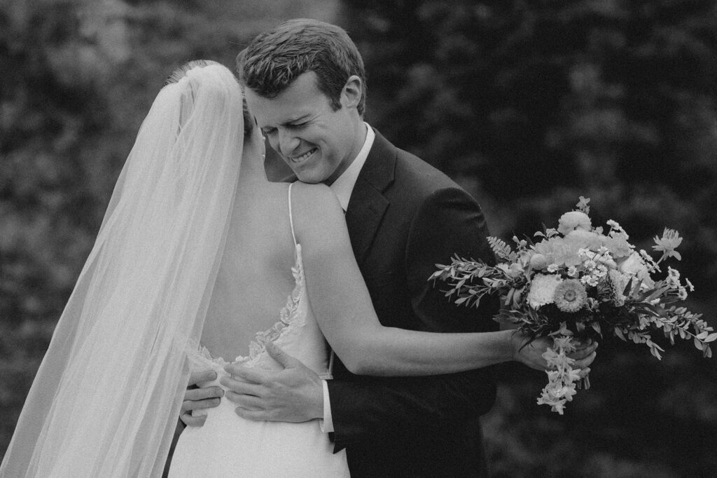 Black and white of groom holding bride and crying on wedding day.