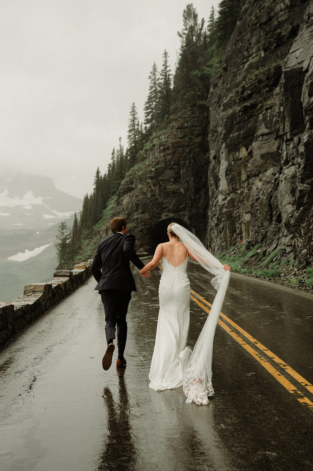 Couple running down going-to-the-sun road in Montana. Road is wet with rain.