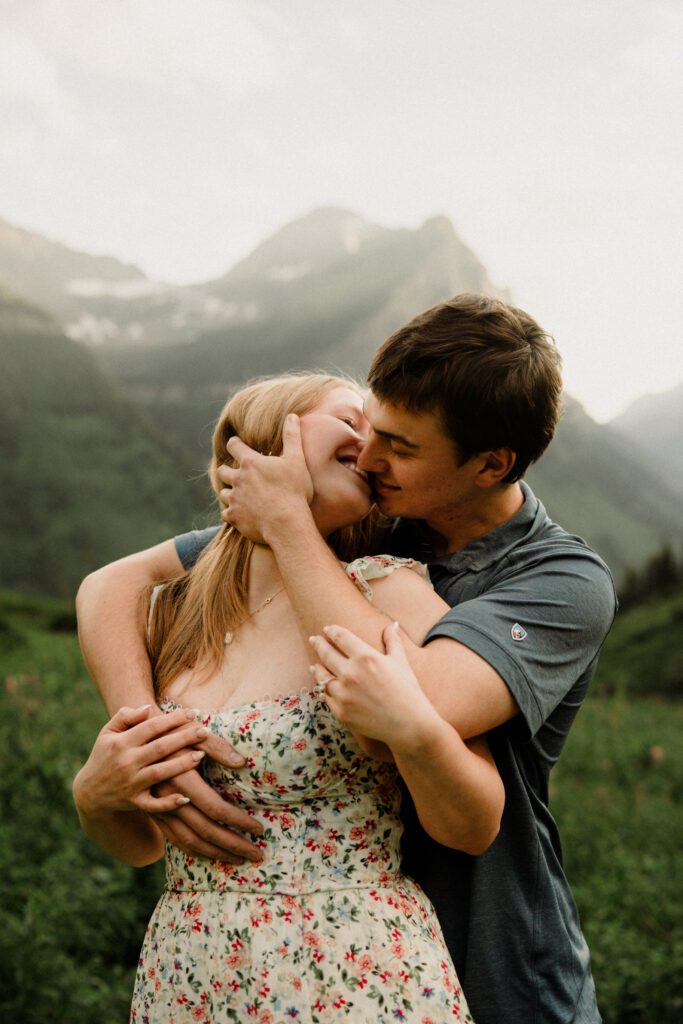 Man kissing woman during their Glacier National Park engagement session! They romped around the amazing Going-to-the-Sun Road, and some of the highlights are in Logan Pass! 
