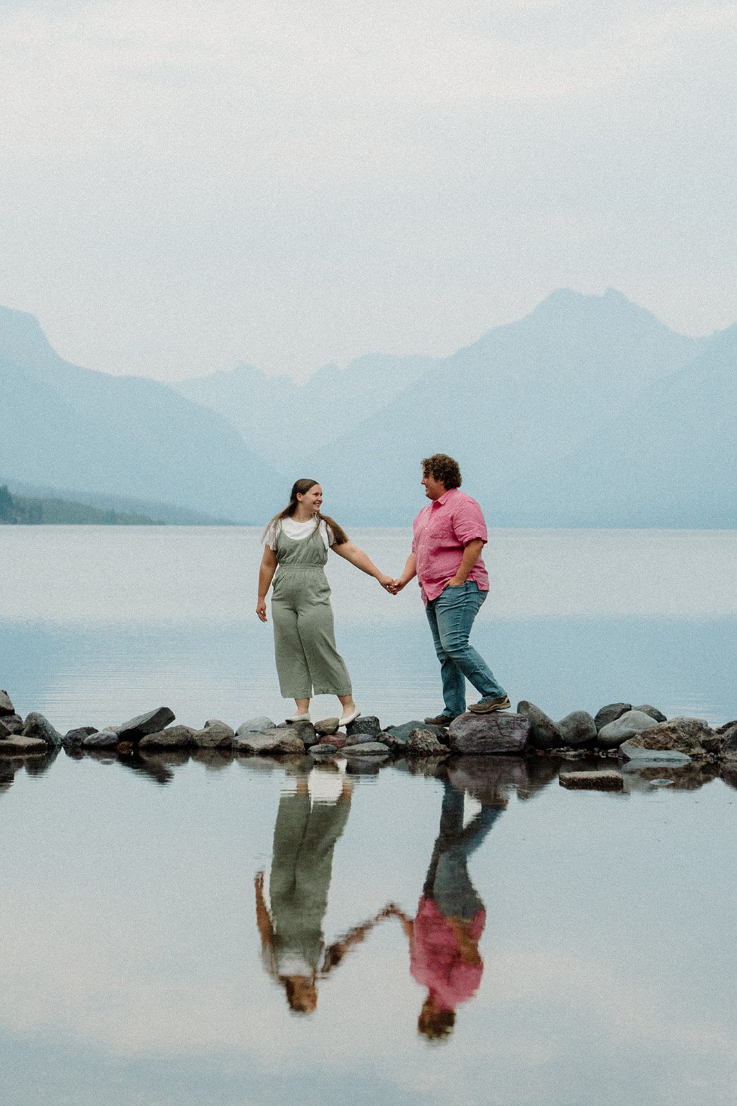 Engagement photos in Glacier National Park with couple walking over water on rock steps.
